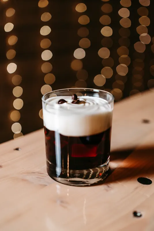 Cocktail mit Schaumhaube auf einem Holztisch vor Lichterketten