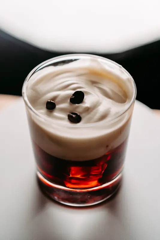 Cocktail im Tumbler mit Sahnehaube und Kaffeebohnen