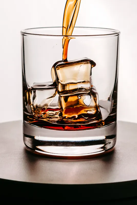 Ein Drink wird über große Eiswürfel in einen Tumbler gegossen