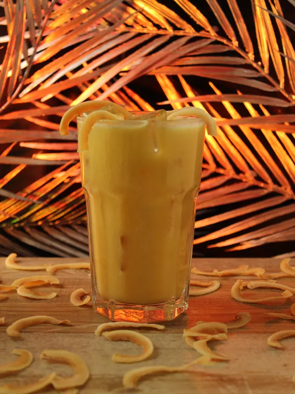 Gelber Cocktail vor einer Kulisse aus Palmblättern
