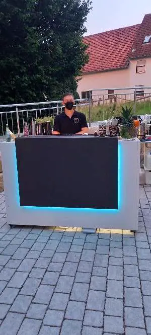 Barkeeper hinter der mobilen Bar mit blauer LED-Beleuchtung am Abend