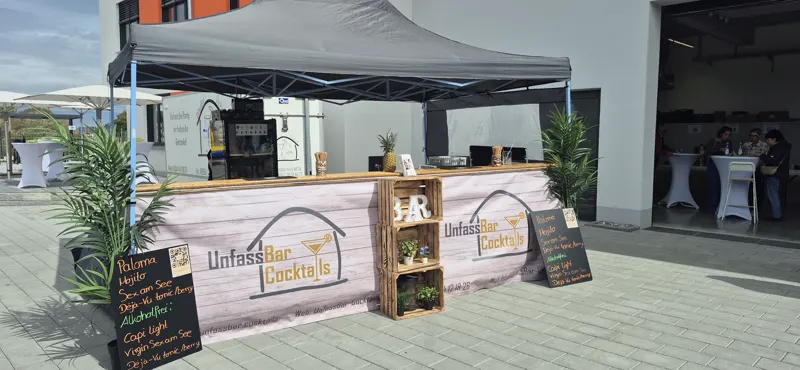 Mobile Bar mit UnfassBar-Cocktails-Banner und Getränketafeln unter einem Pavillon im Freien