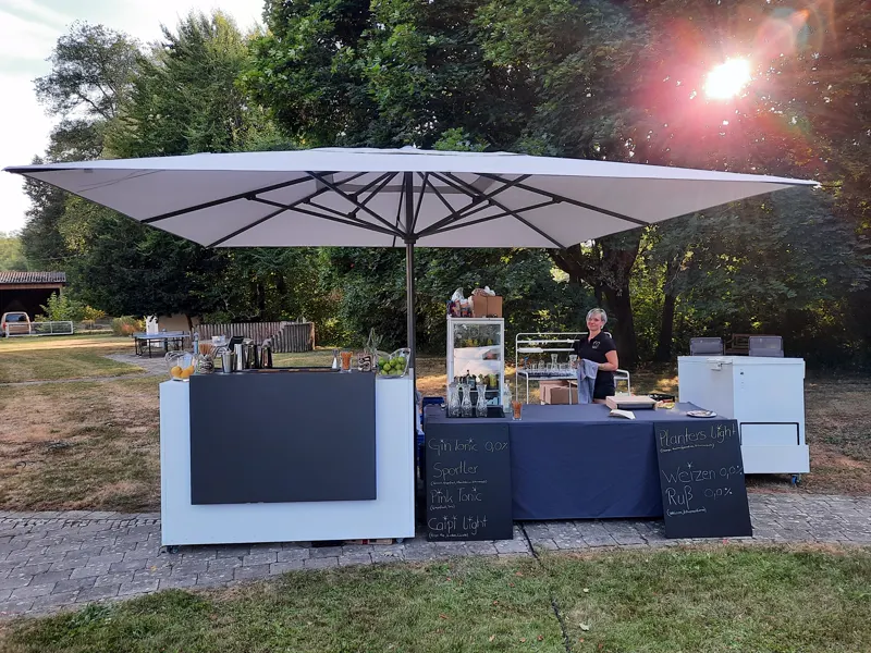 Mobile Cocktailbar unter einem großen Sonnenschirm bei einer Feier im Freien