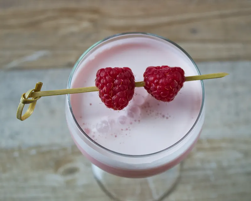 Rosafarbener Cocktail mit Himbeeren am Spieß