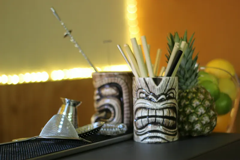 Tiki-Becher mit Strohhalmen, Ananas und Limetten an der Bar